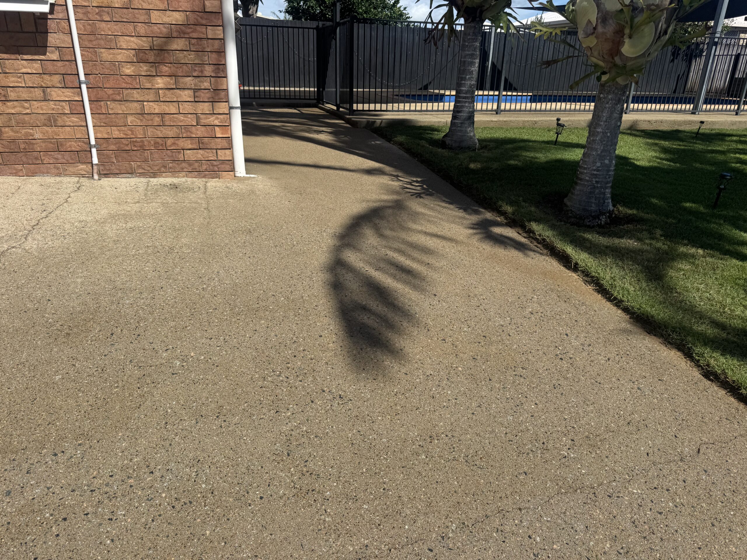 House and driveway areas in Bucasia, with concrete beside a brick wall and pool fence