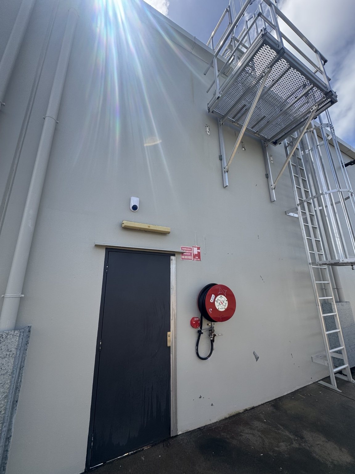 Building wall, dark door and red hose reel at the Anchor Safe rust-cleaning project in North Mackay