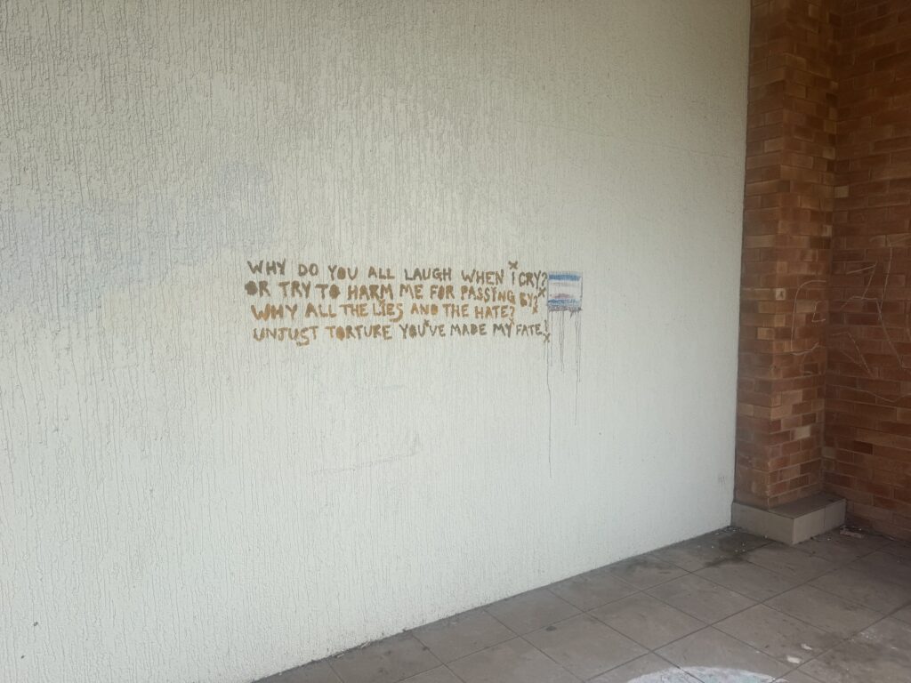 Writing and coloured marks on a cream textured exterior wall before graffiti removal