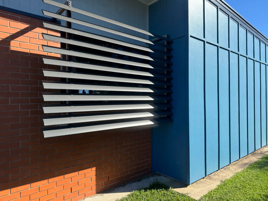 Dark horizontal exterior louvres beside red brick and blue cladding
