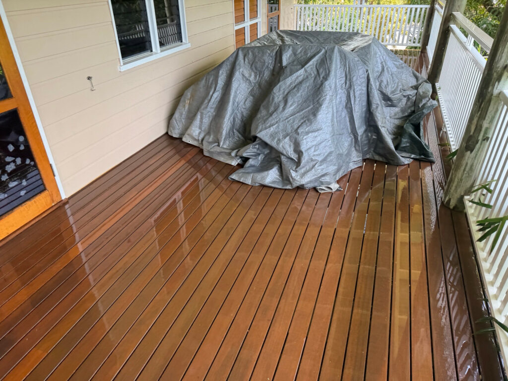 Wet timber deck boards with outdoor furniture covered by a grey tarp