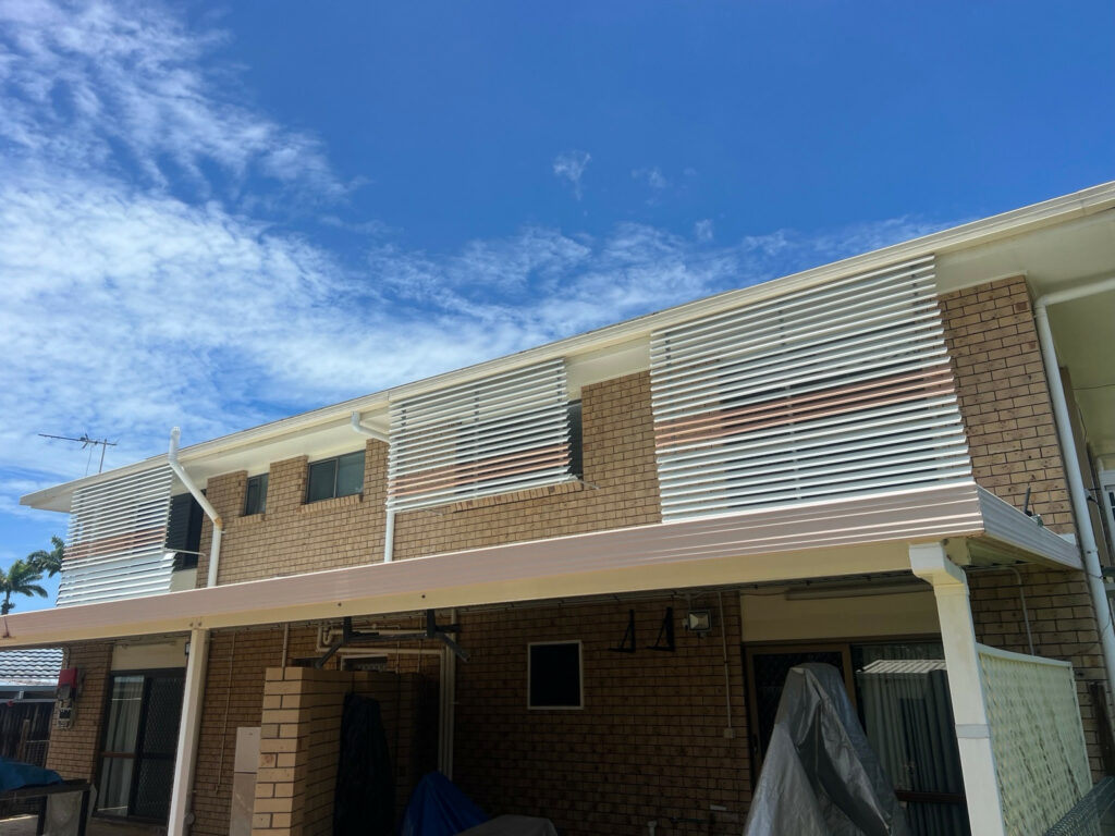 Pale slatted exterior window awnings on a two-storey brick house