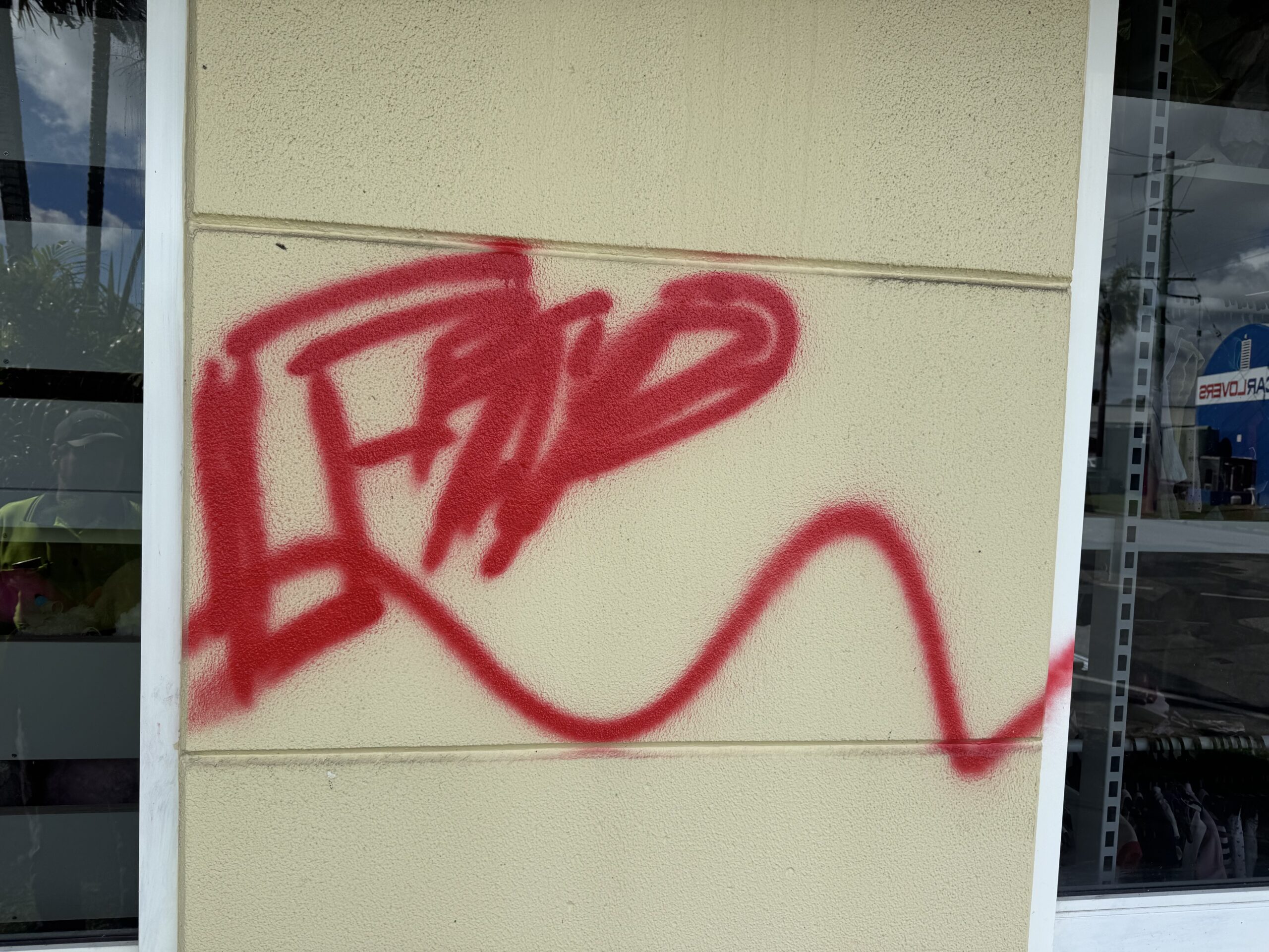 Red spray-painted graffiti on a cream textured wall between shopfront windows